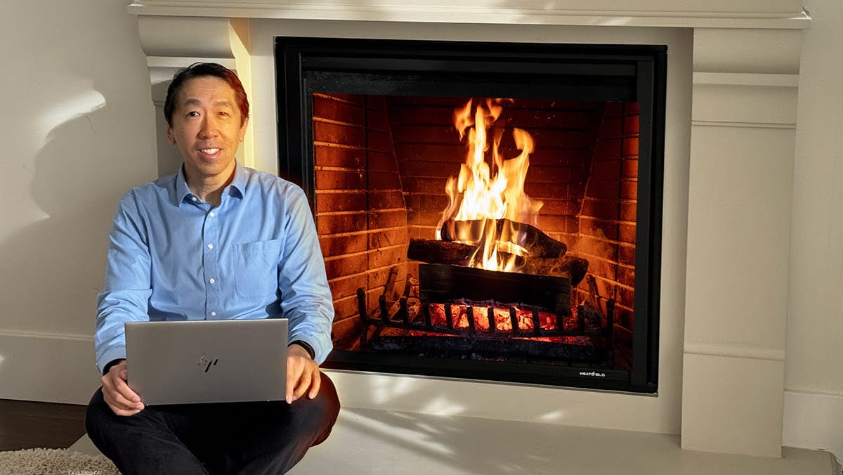 Andrew Ng holding a computer while sitting next to a chimney